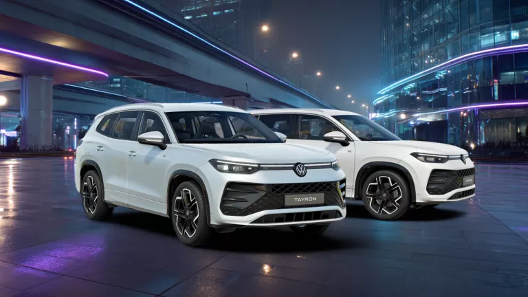 Zwei weiße VW Tayron R-Line nebeneinander vor einer beleuchteten urbanen Kulisse bei Nacht