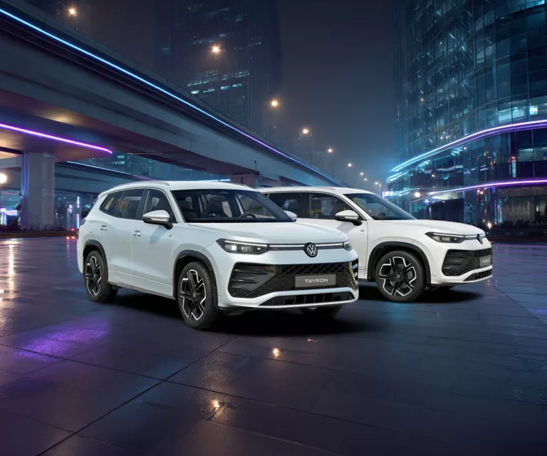 Zwei weiße VW Tayron R-Line nebeneinander vor einer beleuchteten urbanen Kulisse bei Nacht