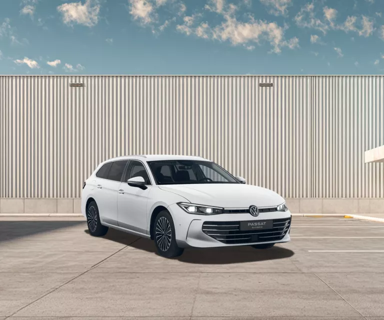Weißer VW Passat steht auf einem leeren Parkplatz vor einer großen, hellen Wellblechwand unter blauem Himmel mit wenigen Wolken.