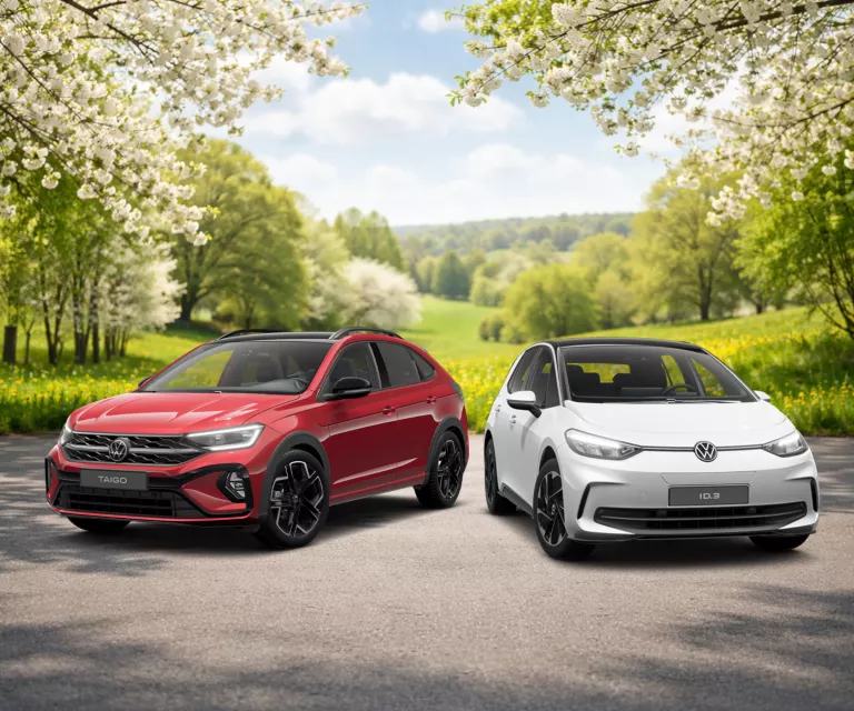 Frühlingshafte Landschaft mit blühenden Bäumen und grüner Wiese im Hintergrund, davor VW Taigo in Rot und ID.3 in Weiß.