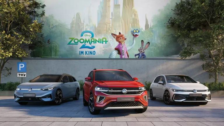 Drei Volkswagen Modelle parken vor einer Betonmauer. Im Hintergrund ist das Motiv des Kinofilms Zoomania 2 zu sehen. 