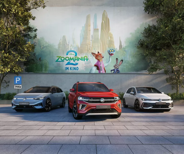 Drei Volkswagen Modelle parken vor einer Betonmauer. Im Hintergrund ist das Motiv des Kinofilms Zoomania 2 zu sehen. 