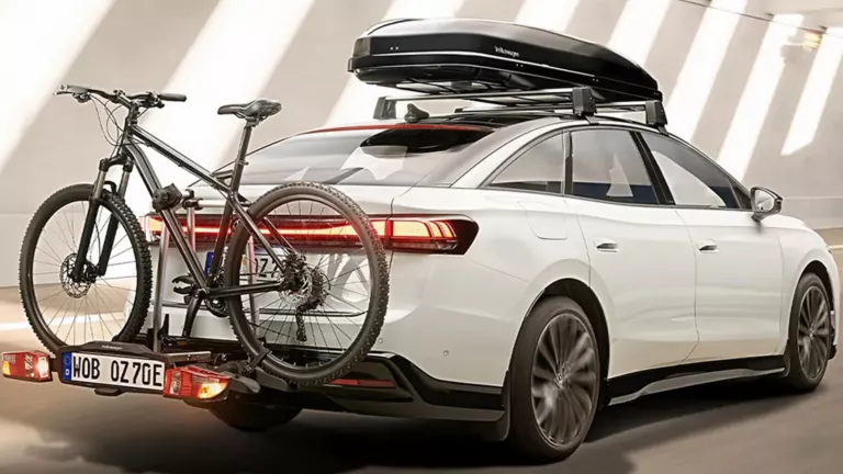 Weißes Auto mit schwarzem Fahrradträger am Heck und schwarzem Dachbox-Zubehör in moderner Garage