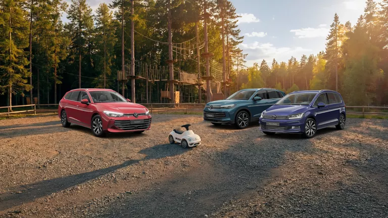 Drei VW Modelle stehen bei untergehnder Sonne vor einem Kletterpark auf einem Parkplatz im Wald.