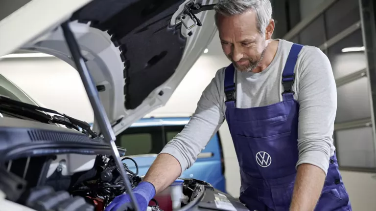 Ein Servicemitarbeiter begutachtet den Motorraum eines Volkswagen Fahrzeugs.