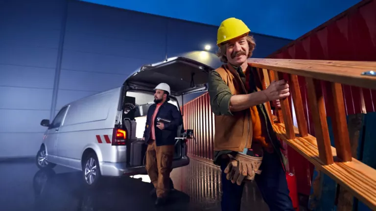 Handwerker der eine Leiter aus einem VW T5 Transporter trägt.