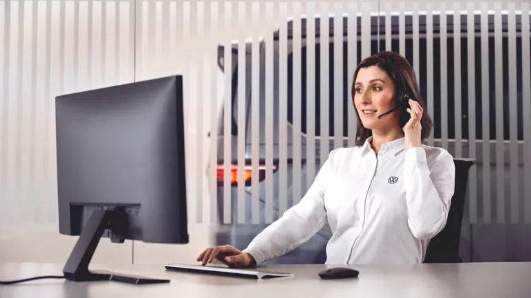 Frau sitzt am Schreibtisch und arbeitet mit Headset.