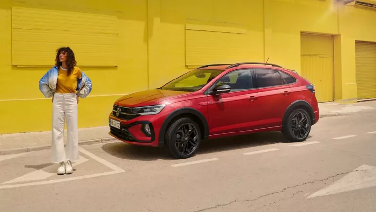 Una mujer junto a un Volkswagen Taigo rojo parado junto una pared amarilla