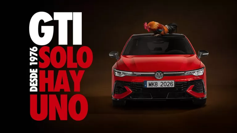 Un Volkswagen rojo visto de frente con un gallo encima y el fondo oscuro