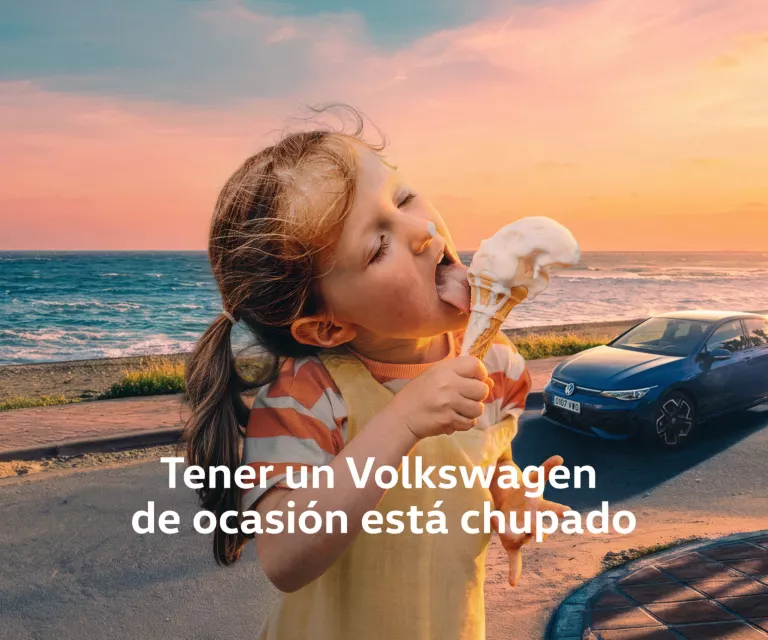 Una niña disfrutando de un cucurucho con un Volkswagen azul detrás en la playa