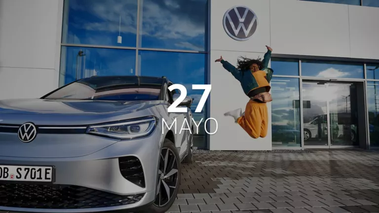 Una chica saltando feliz delante de un concesionario Volkswagen junto un coche plateado