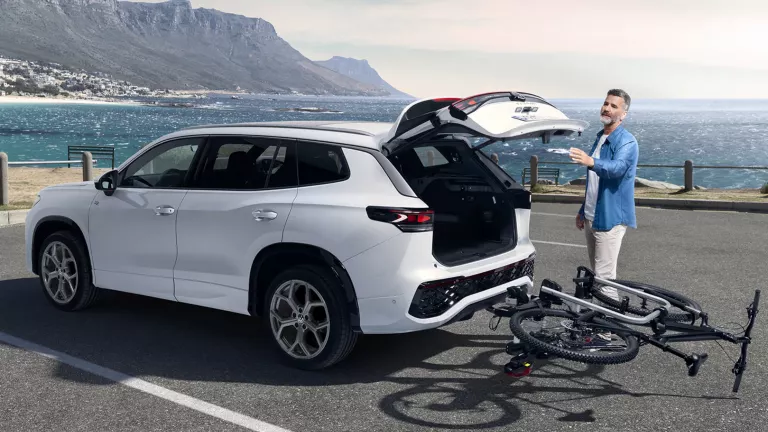 Ein Mann schließt den Kofferaum seines weißen VW T-Roc. An der Anhängerkupplung ist ein Fahrradanhänger montiert das Fahrrad ist umgeklappt, damit der Kofferraum zugeht.