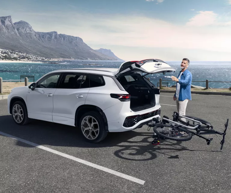 Ein Mann schließt den Kofferaum seines weißen VW T-Roc. An der Anhängerkupplung ist ein Fahrradanhänger montiert das Fahrrad ist umgeklappt, damit der Kofferraum zugeht.
