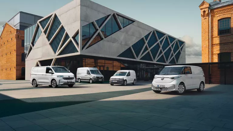 Volkswagen Nutzfahrzeuge ID. Buzz, Caddy, Transporter und Crafter parken auf einem Parkplatz vor einem modernen weißen Bürogebäude.