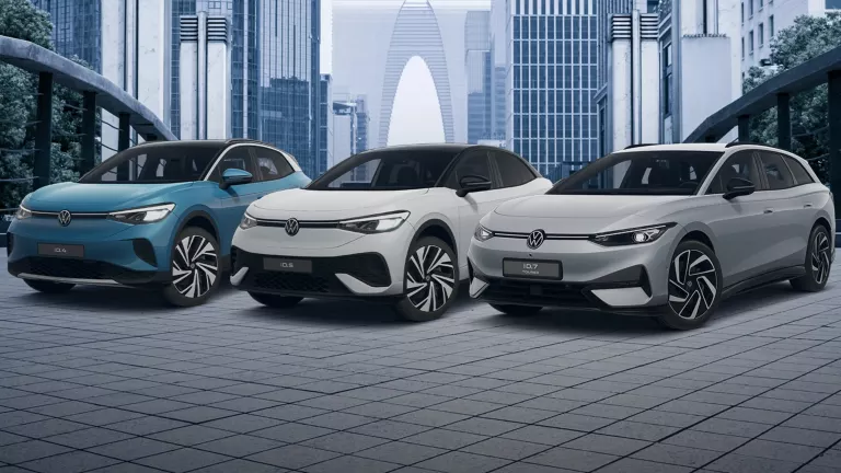 Ein blauer VW ID.4, ein weißer VW ID.5 und ein grauer VW ID.7 Tourer stehen auf einer gepflasterten Fläche in einer Stadt.