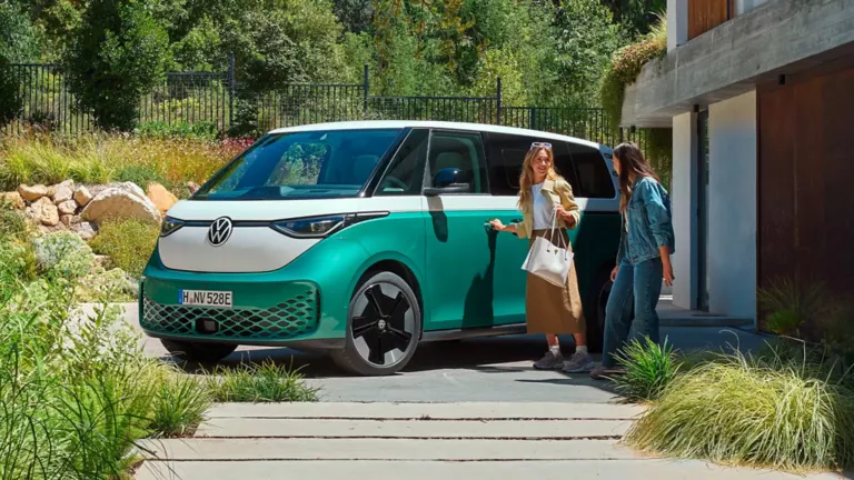 Zwei Frauen steigen in einen Türkisen VW ID. Buzz steigen.