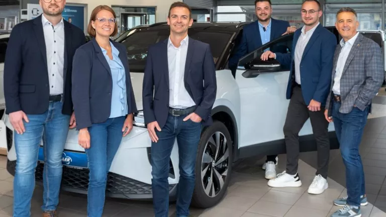 Mitarbeiter des aAutohauses im Verkaufsraum vor einem weißen VW