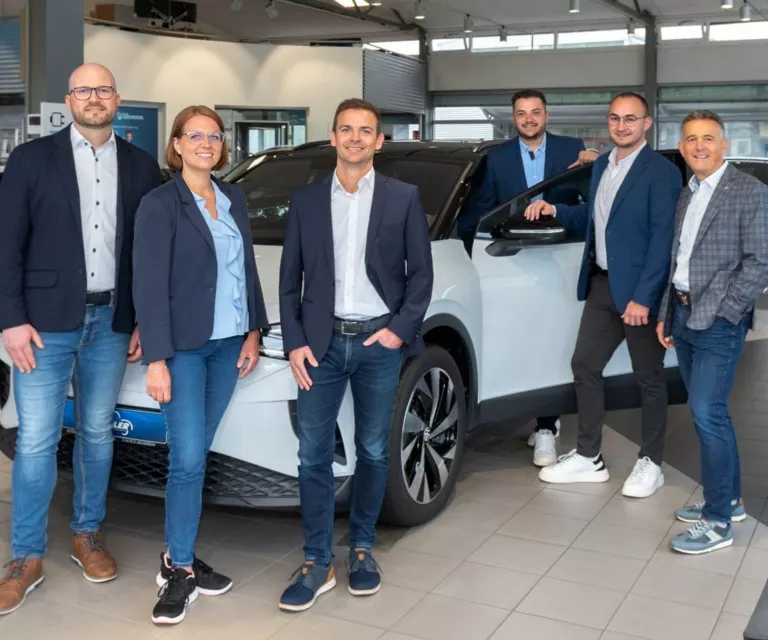 Mitarbeiter des aAutohauses im Verkaufsraum vor einem weißen VW