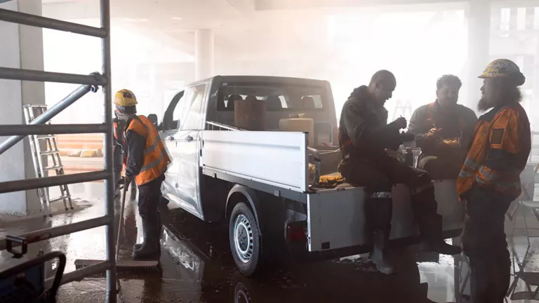 Mehrere Bauarbeiter pausieren um einen VW Crafter Pritschenwagen.