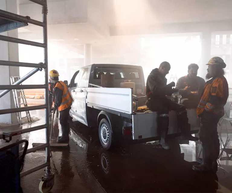 Mehrere Bauarbeiter pausieren um einen VW Crafter Pritschenwagen.