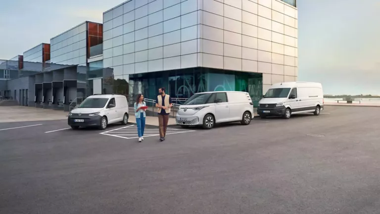 Ein Mann und eine Frau laufen auf einem Parkplatz auf dem Volkswagen Nutzfahrzeuge parken.