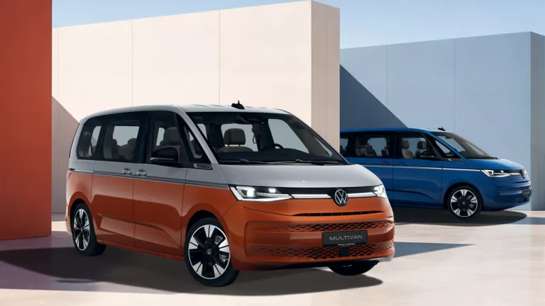 VW Multivan in grauer Lackierung auf Betonfläche vor blühendem Baum und bewölktem Himmel