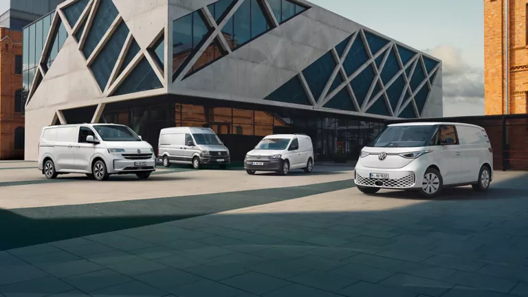 Vier verschiedene VW-Transporter stehen vor einem modernen Gebäude mit geometrischer Architektur.