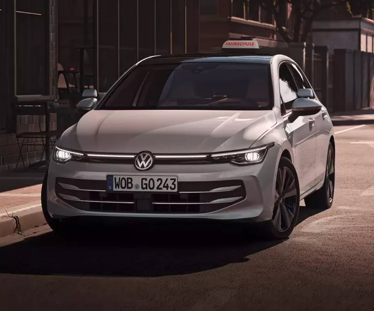 Ein weißer VW als Fahrschulauto umgebaut parkt vor einem Cafe.