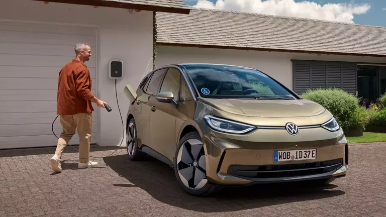 Ein Mann mit einem Ladekabel will seinen geparkten VW ID. 3 laden. 