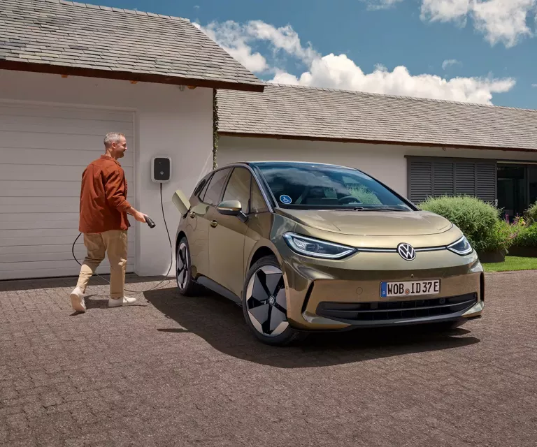 Ein Mann mit einem Ladekabel will seinen geparkten VW ID. 3 laden. 