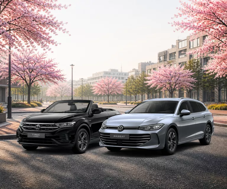 VW T-Roc Cabriolet und Passat Business auf einen Parkplatz mit blühenden Bäumen.
