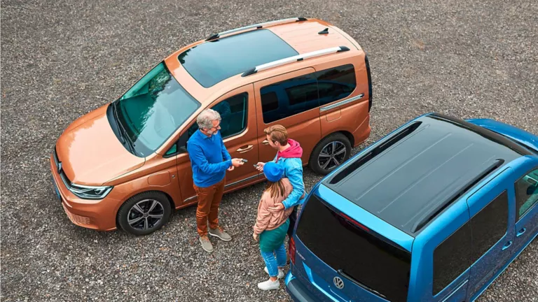 Ein älterer Mann, eine Frau und ein Mann stehen zwischen zwei Volkswagen Caddy Modelle und unterhalten sich.