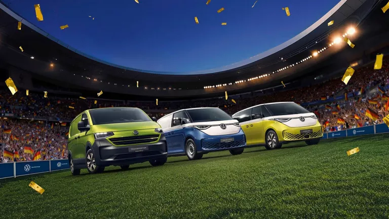 Drei VW Nutzfahrzeuge stehen in einem Vollen Fußballstadion mitten auf dem Rasen.