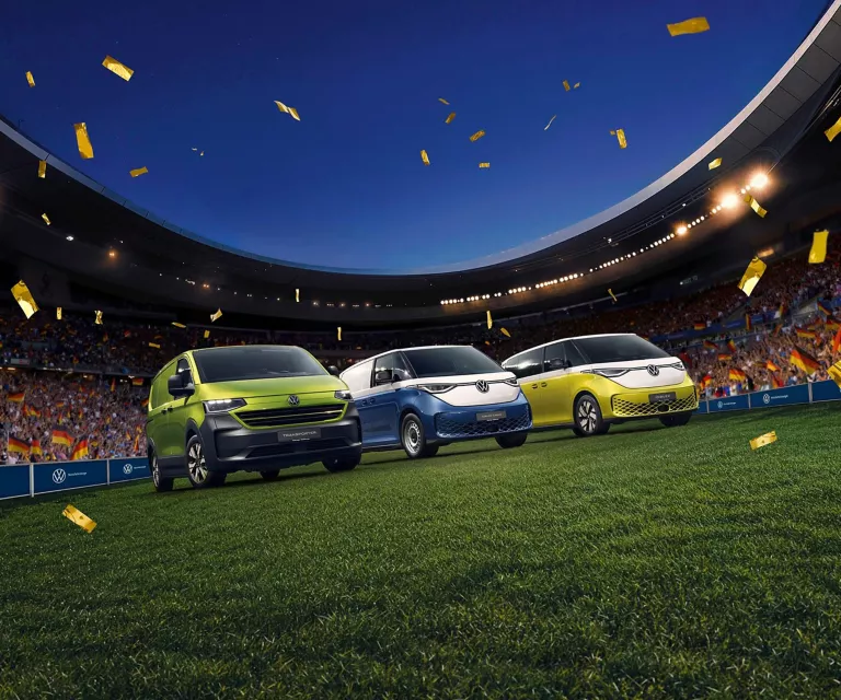 Drei VW Nutzfahrzeuge stehen in einem Vollen Fußballstadion mitten auf dem Rasen.