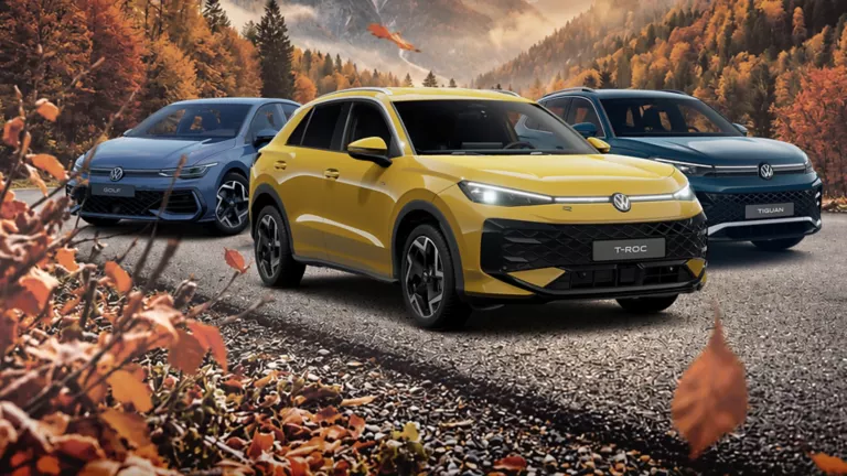 VW Golf, VW T-Roc und VW Tiguan stehen nebeneinander auf einer Straße. Im Hintergrund sieht man eine Bergkette und einen Wald der schon Herbstfarben angenommen hat.