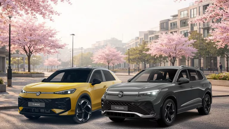 Ein grauer VW Tiguan und ein gelber VW T-Roc stehen auf einem asphaltiertem Weg in einer Stadt mit blühenden Bäumen.