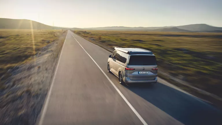 Ein grauer VW Transporter fährt auf einer Landstraße in die Ferne.