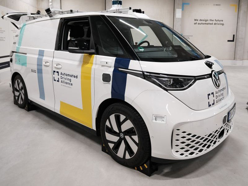 A white Volkswagen van branded with the “Automated Driving Alliance” stands beside a wall declaring, “We design the future of automated driving”—a clear statement of collaborative innovation.