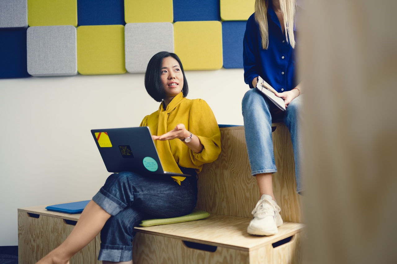 Colleagues discussing ideas while working with a laptop in a modern office, representing women in tech at CARIAD.