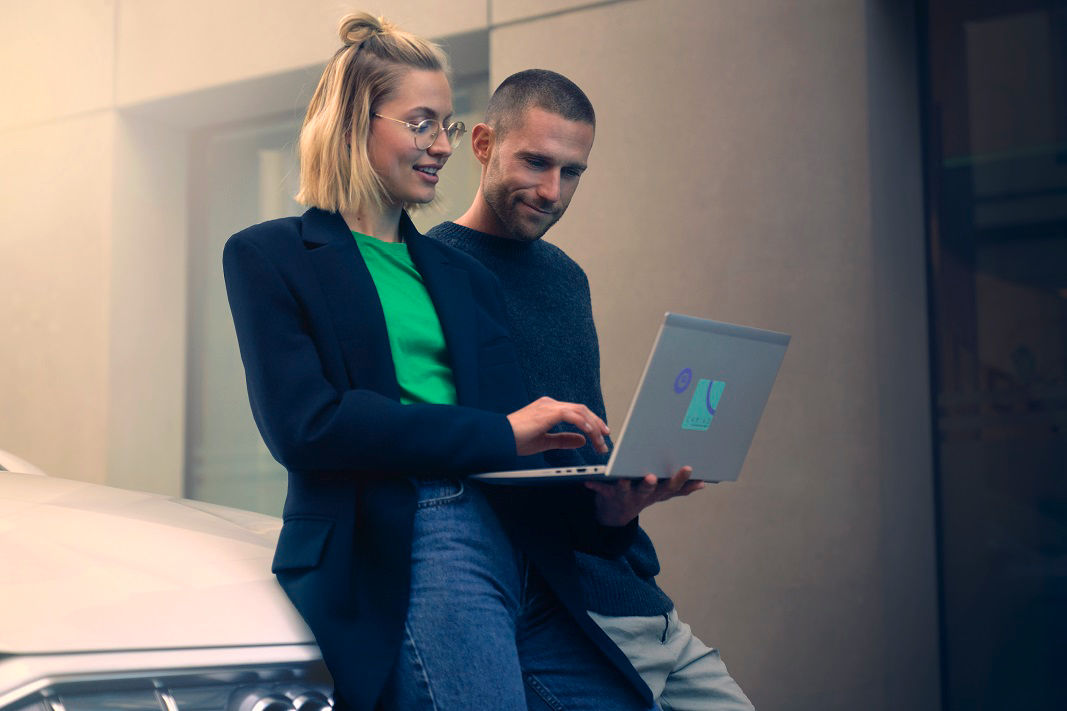 two people with a laptop in front of a car