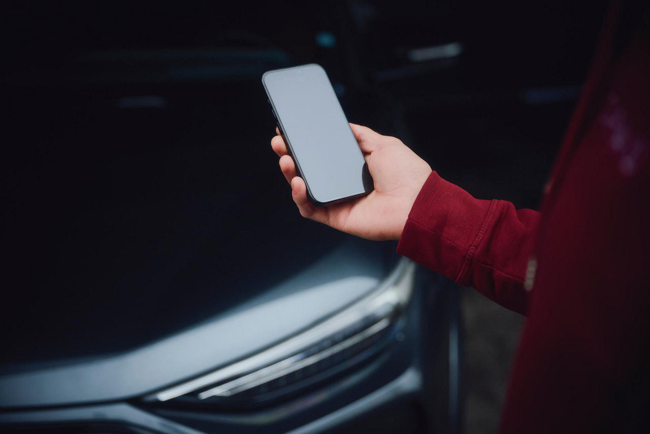 A person in a red shirt holds a smartphone near the front of a car, symbolizing the intersection of mobile tech and automotive design.