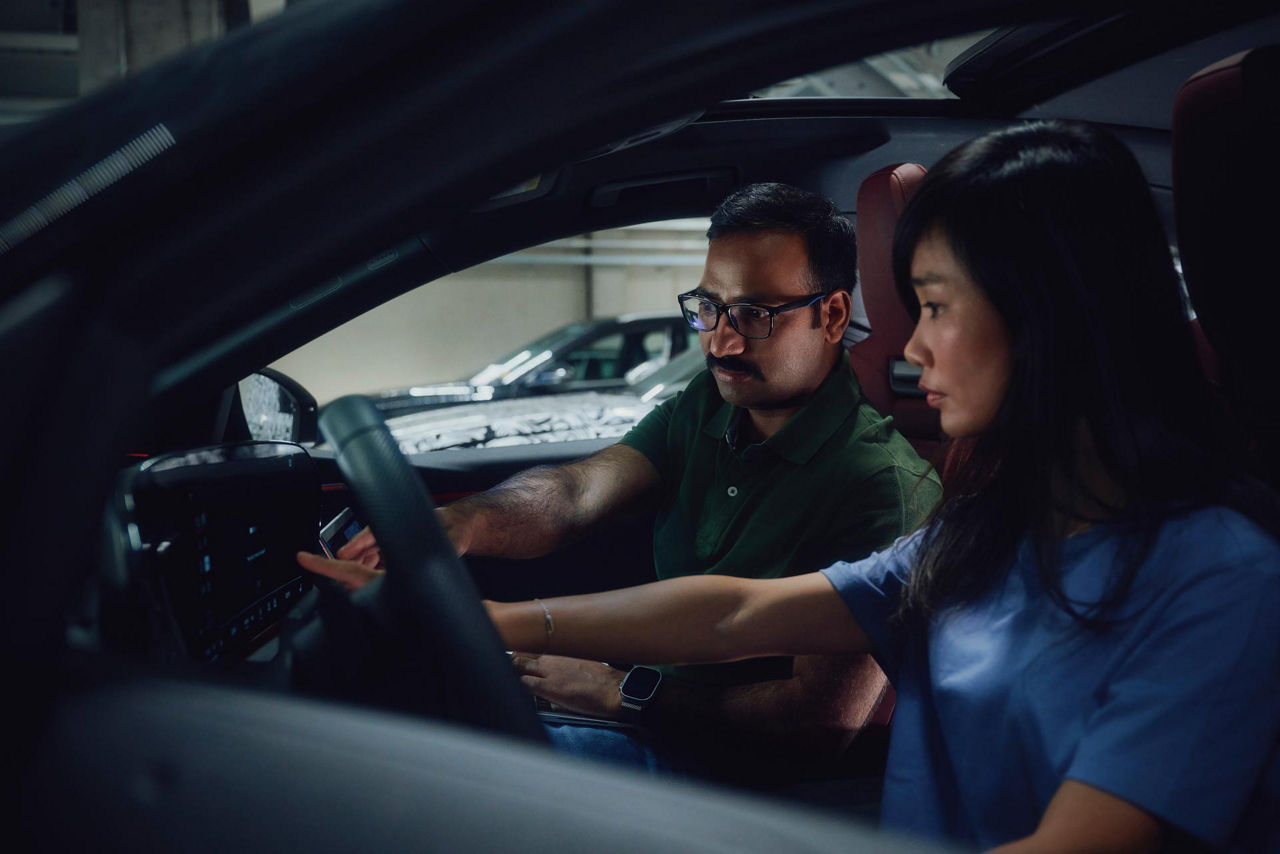 Two people sitting in the front seats of a car, interacting with the dashboard controls.