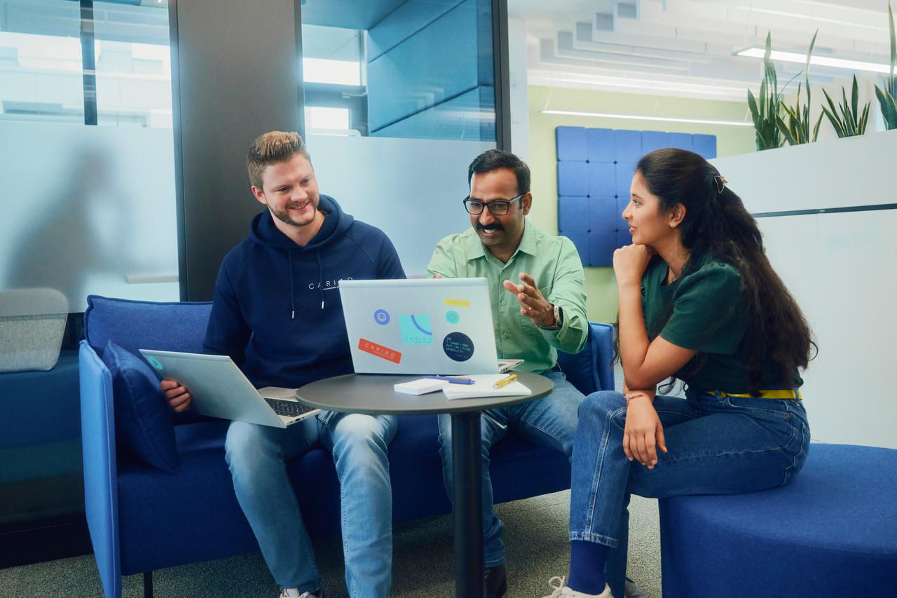 CARIAD employees collaborating around a laptop in a modern office workspace.