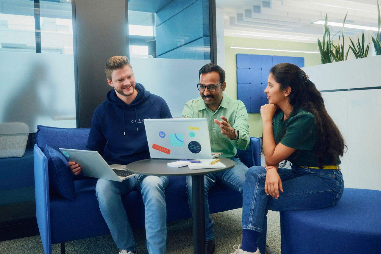 Group of  three working employees in front of a laptop in an office set up discussing.