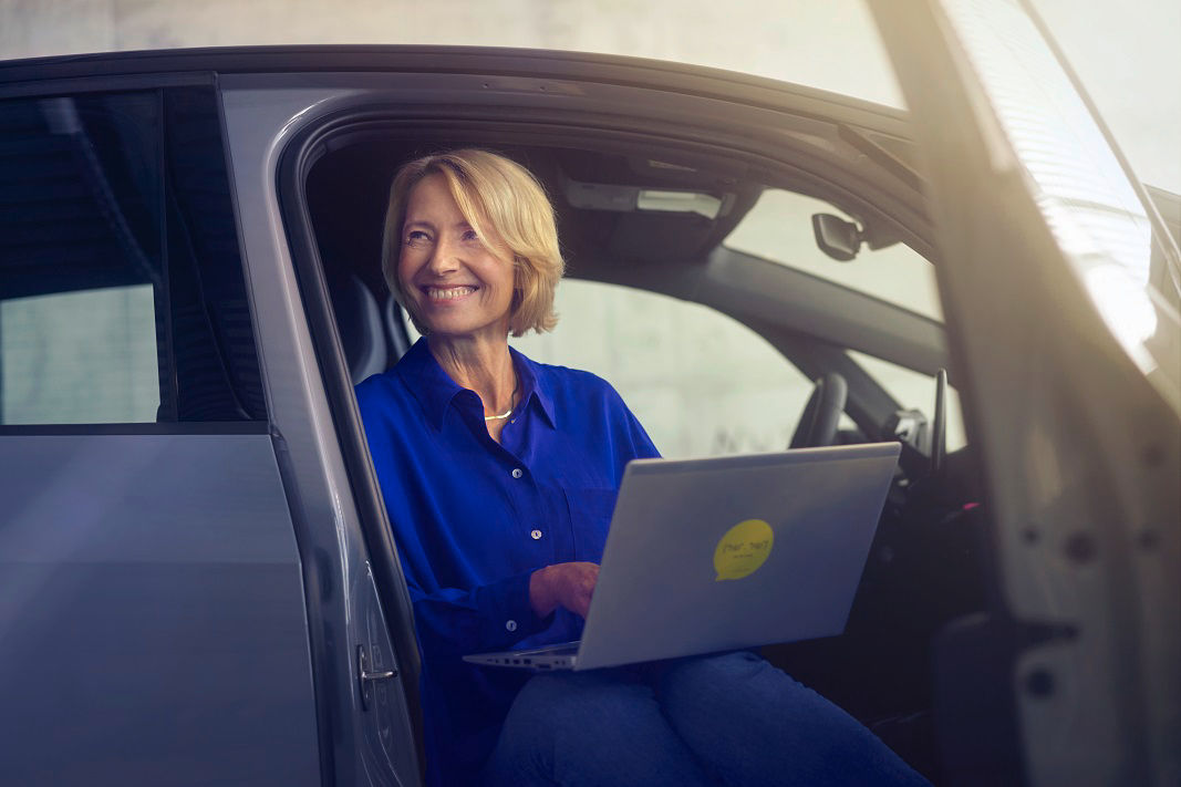 smiling-woman-in-blue-blouse-sitting-in-car-door-with-laptop