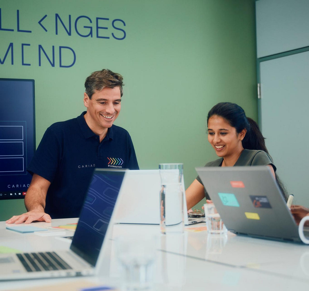 Team of colleagues collaborating in a modern meeting room with laptops and a presentation screen.