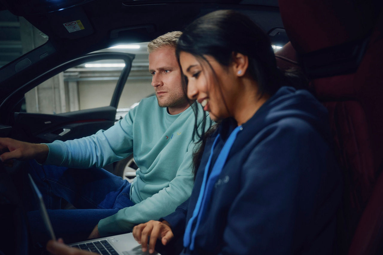Two young professionals working together inside a car while reviewing information on a laptop.