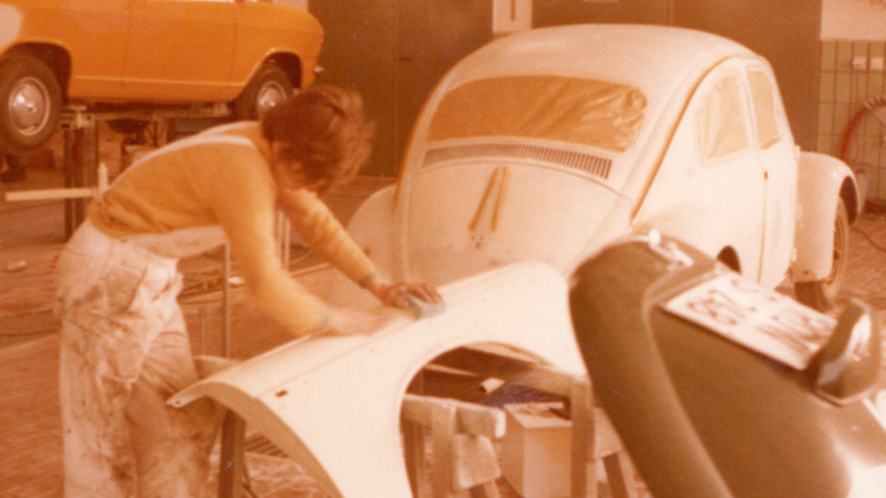 Sepiafarbenes Foto von einem Werkstattmitarbeiter, der an einem VW Käfer arbeitet