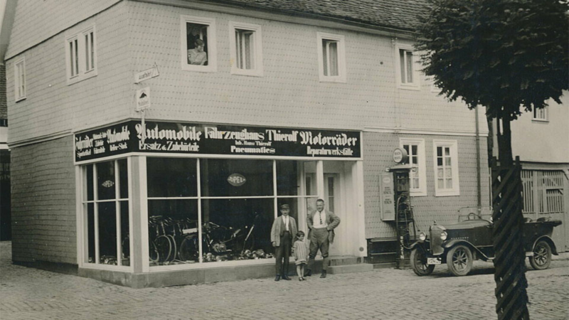 Schwarz-Weiß-Fotografie von Autohaus-Gründer Hans Thierolf mit Familie vor dem Fahrzeughaus Thierolf in Höchst im Odenwald