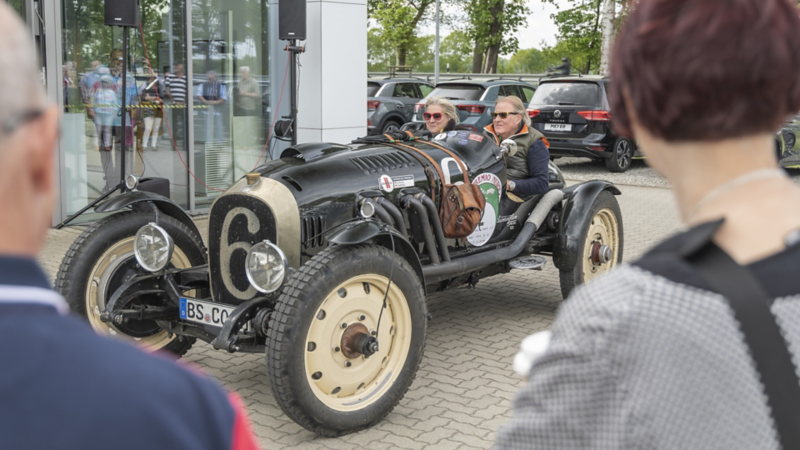 Zwei Menschen im Oldtimer vor dem Autohaus